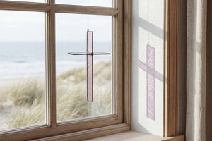 Warm Stone Cross Suncatcher hanging in a window and catching natural light