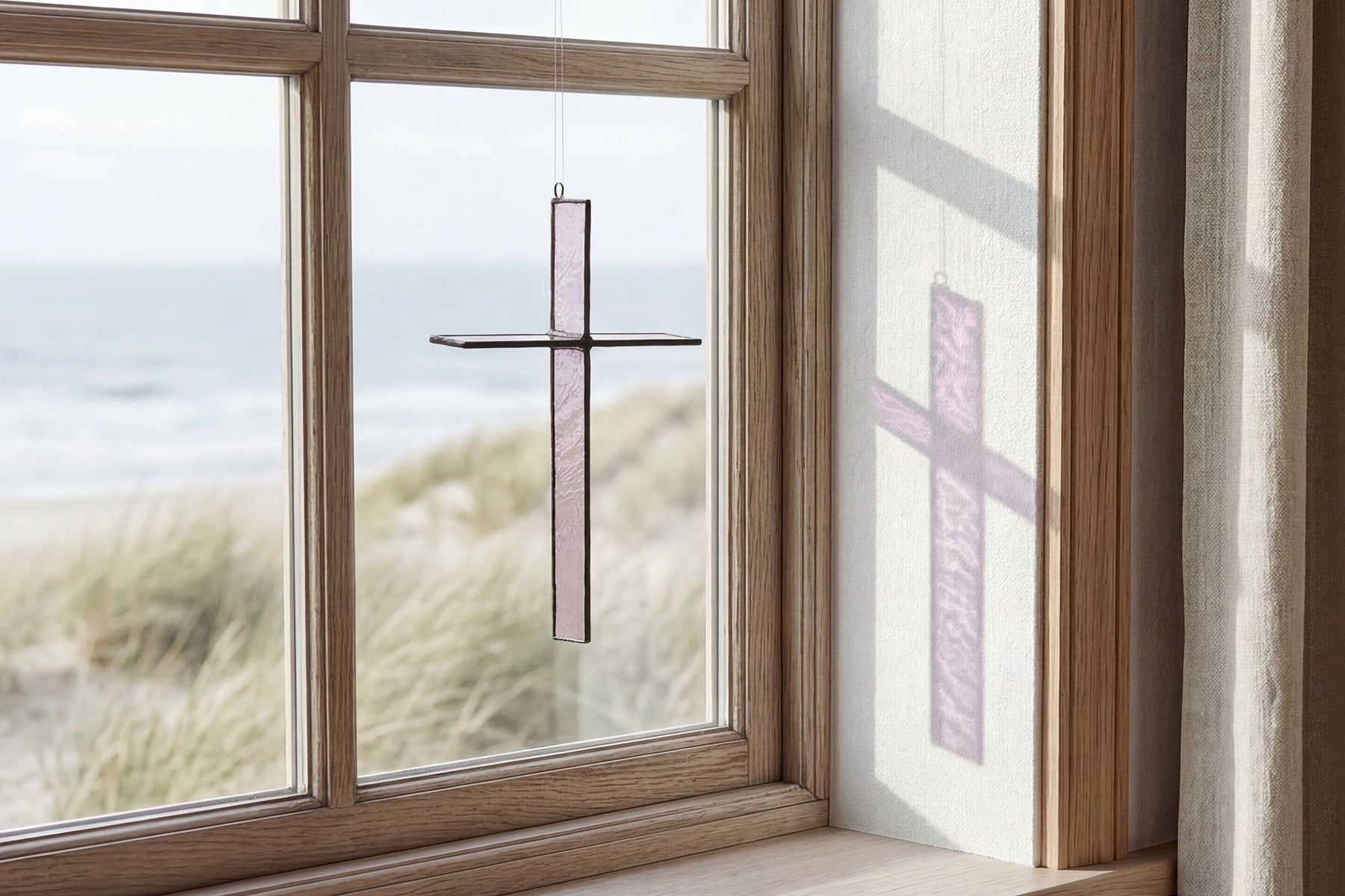 Rose Mist Cross Suncatcher hanging in a window and catching natural light