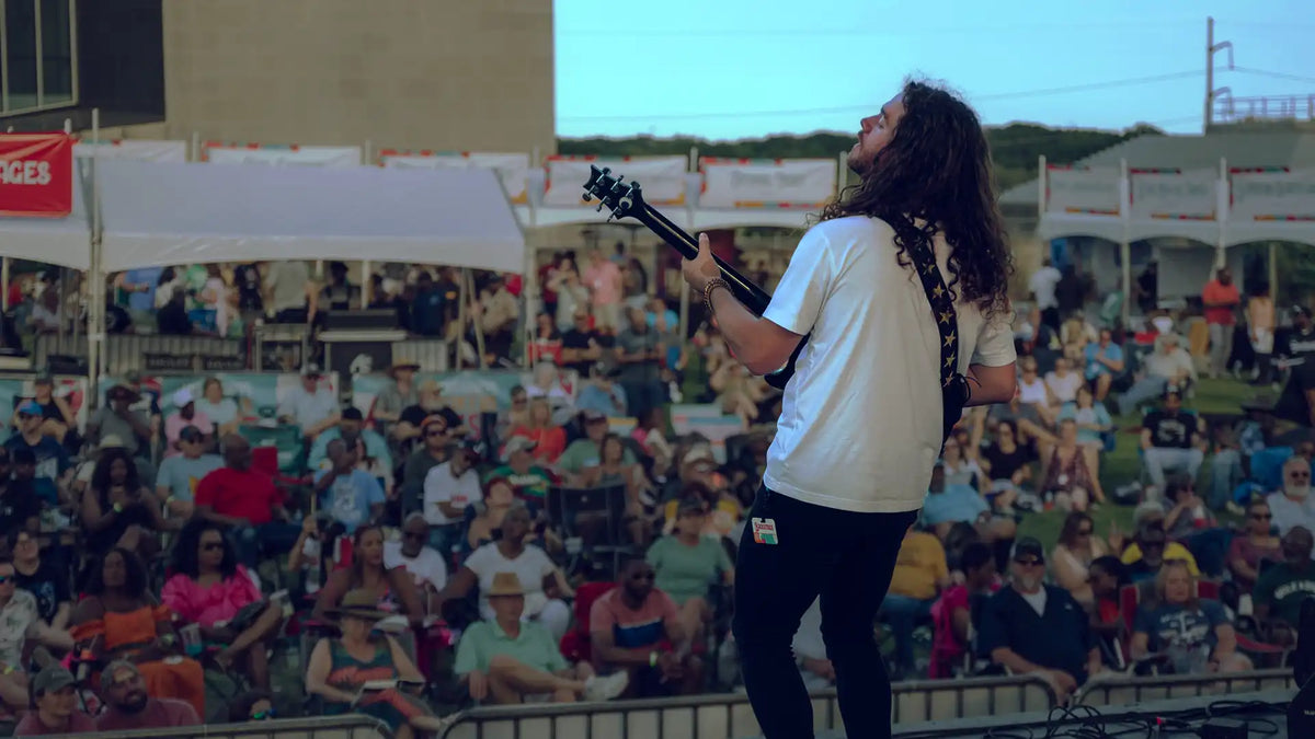 Musician playing an electric guitar on stage facing a large outdoor audience